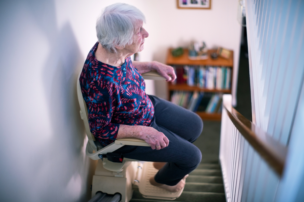 A woman uses a stair lift on her home staircase.