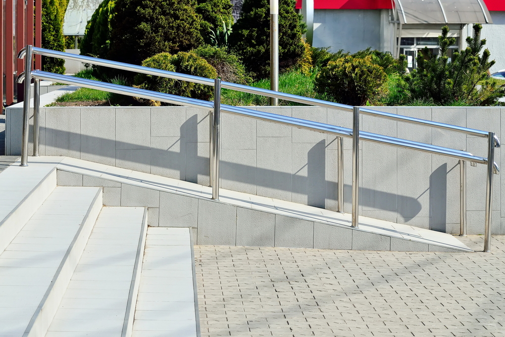 A permanent concrete wheelchair ramp with a metal hand railing.